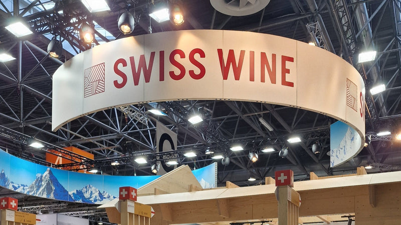 The Swiss Wine stand at ProWein 2024 in Düsseldorf, a red and white SWISS WINE ring above a light wood stand with Swiss flags.