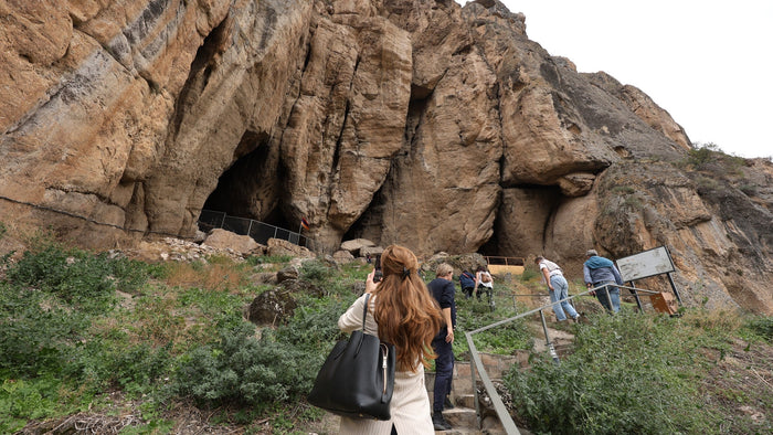 The red cliff above the Arpa River in Vayots Dzor that holds the Areni-1 cave, with a small figure on the path below for scale. Photo: Bogossi Production