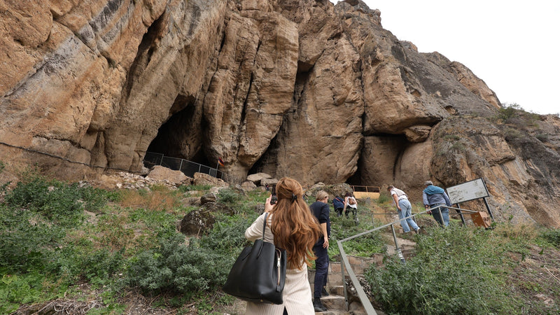 The red cliff above the Arpa River in Vayots Dzor that holds the Areni-1 cave, with a small figure on the path below for scale. Photo: Bogossi Production