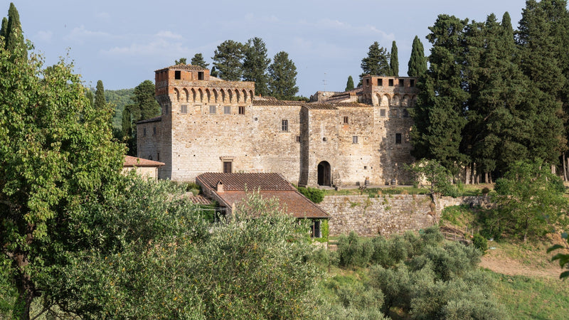 Aerial view of Castello del Trebbio, the honey-stone Tuscan fortress with its square tower ringed by cypress, olive terraces and Chianti Rufina vineyards, headquarters of Famiglia Casadei.