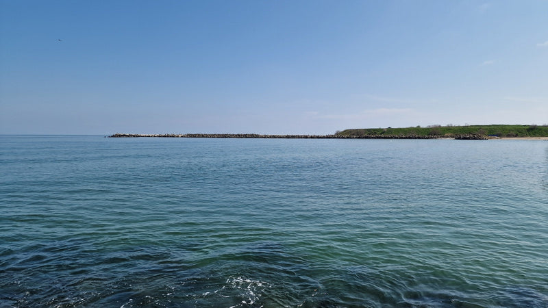 The Black Sea off Constanța, calm blue-green water and a rocky breakwater under a clear spring sky.