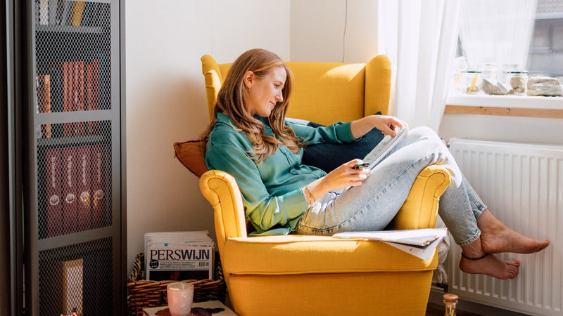 Margot van Lieshout curled up reading a colour-coded WSET study syllabus in a mustard-yellow armchair beside a shelf of wine books.
