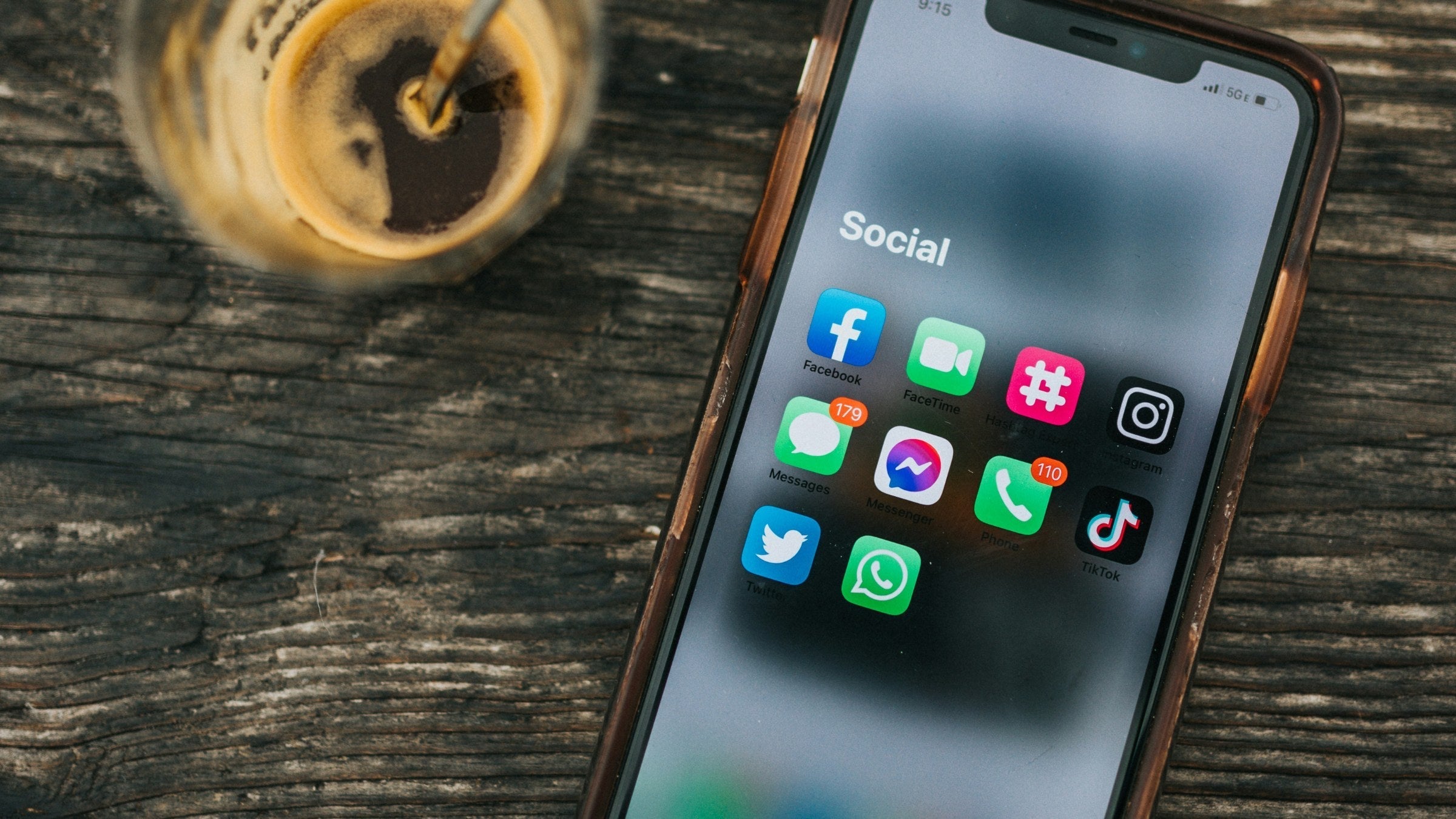 A person scrolling a social media feed on their phone with a glass of wine within reach, the everyday scroll moment before any platform strategy exists, composed as the article hero. Photo: Nathan Dumlao (Unsplash)