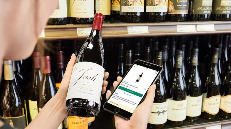 A person relaxing at home reading a wine webshop on a laptop with a glass of wine nearby, hesitating over a purchase.