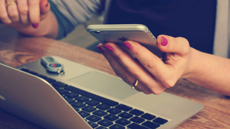 A shopper's phone showing a wine webshop product page, thumb hovering over the buy button just before deciding.