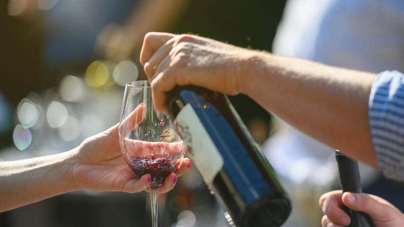 A hand pouring wine at a lived-in table in the last of the evening light, an atmospheric real-life scene rather than a studio shot