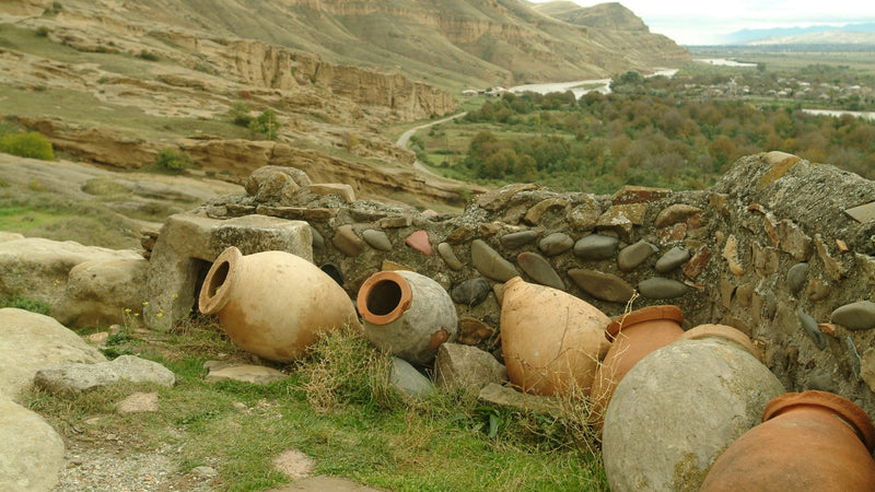 Clay qvevri wine vessels lying by an old stone wall above a river valley in Georgia, photo Wines of Georgia