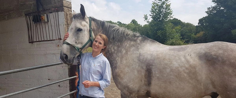 Margot cheek to cheek with a grey dapple horse outside a stable, a nod to the horse-stable and barnyard aromas that Brett throws in wine