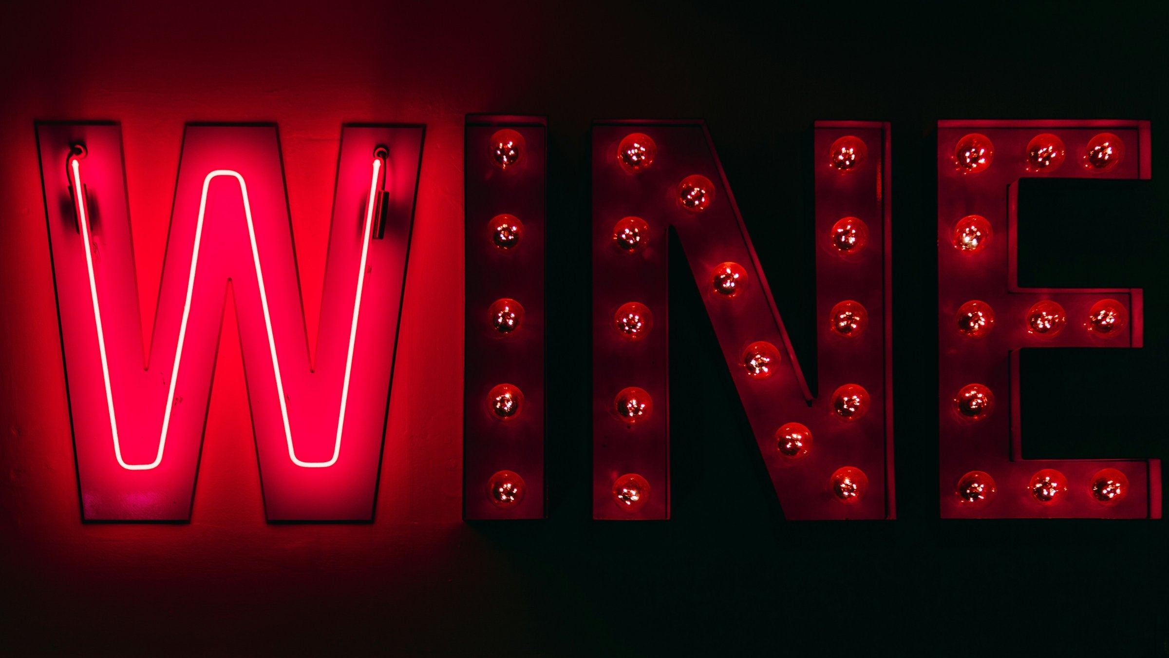 Red neon and marquee light bulb letters spelling WINE against a dark wall