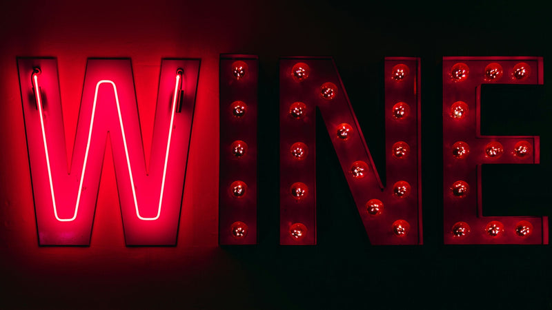 Red neon and marquee light bulb letters spelling WINE against a dark wall