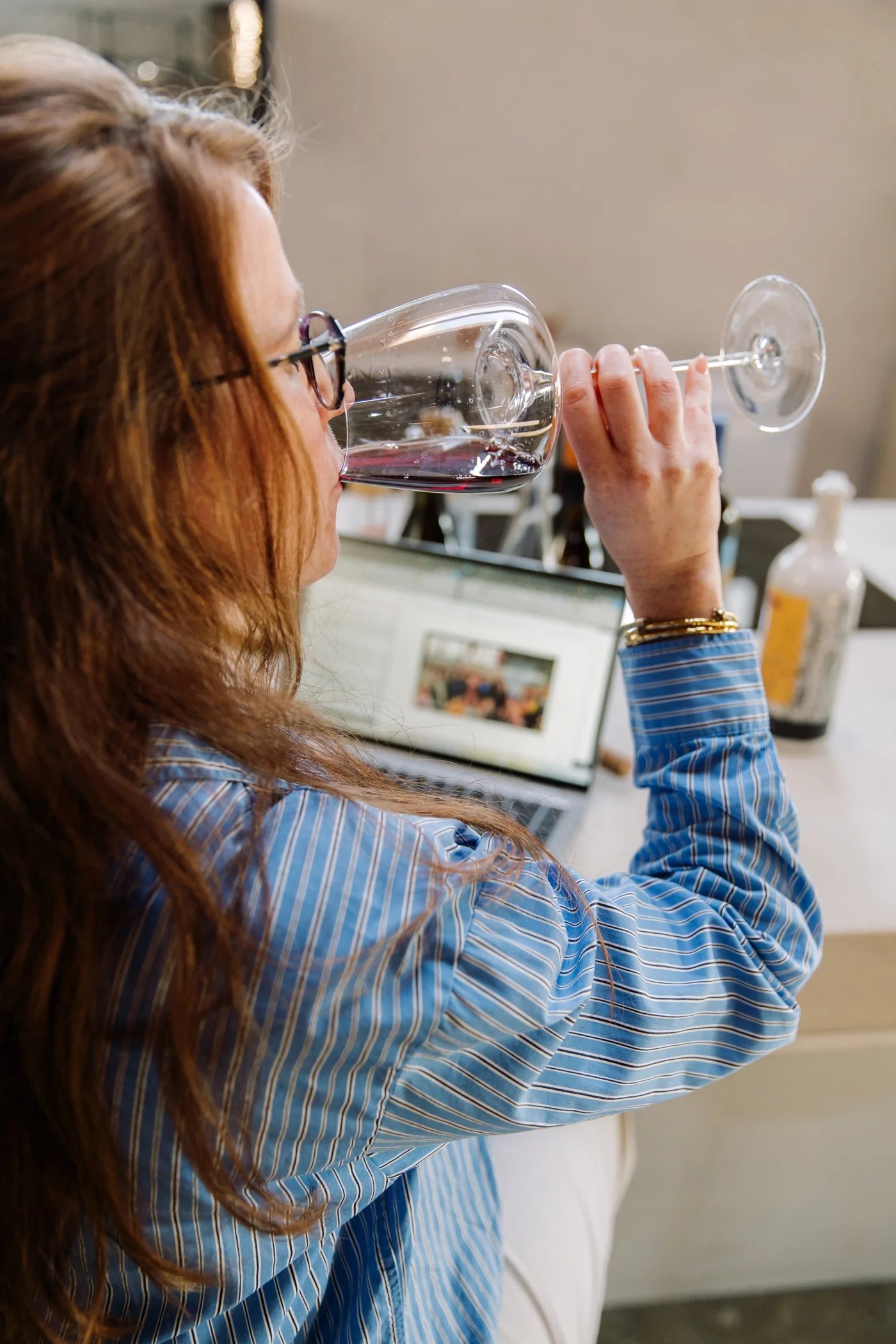 Margot van Lieshout enjoying a glass of red wine at her laptop, working on a wine brand's digital strategy from her home office